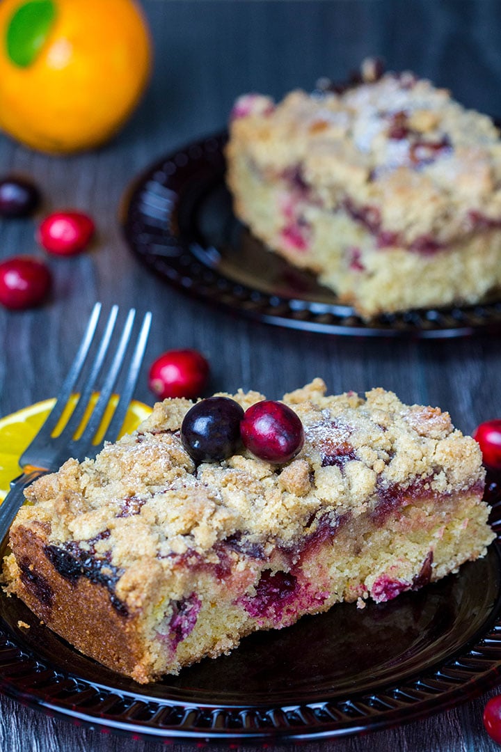 A piece of Cranberry Orange Crumb Cake with cranberries scattered around it on the table