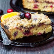 A piece of Cranberry Orange Crumb Cake with cranberries scattered around it in the table