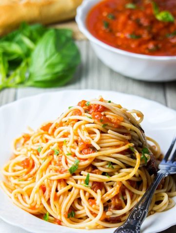 A plate of pasta with marinara sauce with a fork next to it and fresh basil near the dish