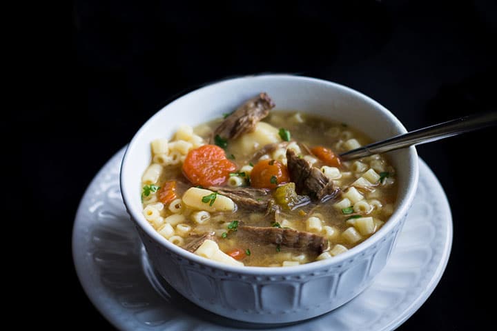 A bowl full of Slow Cooker Beef Brisket Soup with vegetables and small soup pasta added