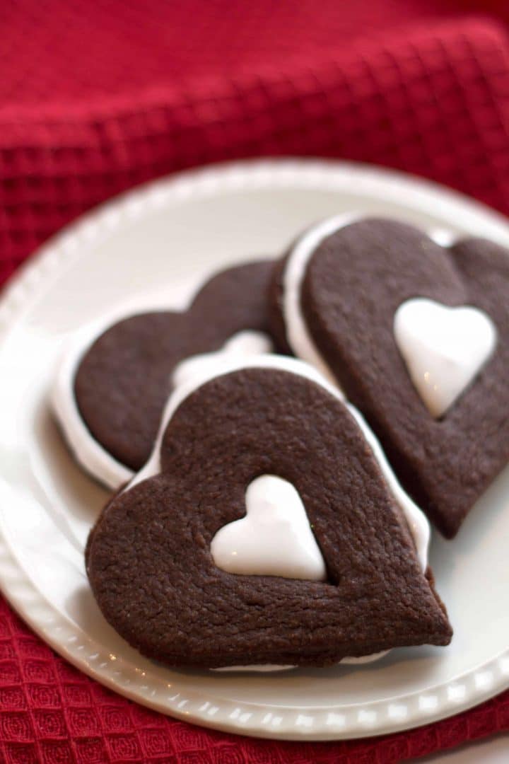 Heart shaped Chocolate Marshmallow Linzer Cookies on a plate with a red background