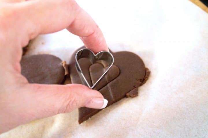 Cookie dough in a heart shape with a small cookie cutter cutting out the center of the heart