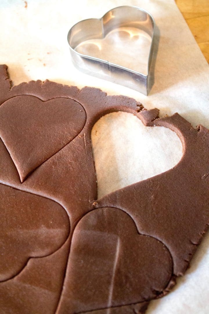 Chocolate cookie dough rolled out with a heart shaped cookie cutter and hearts cut out of the dough