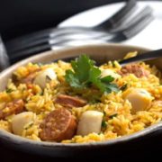 A bowl of scallops and chorizo paella with cutlery in the background