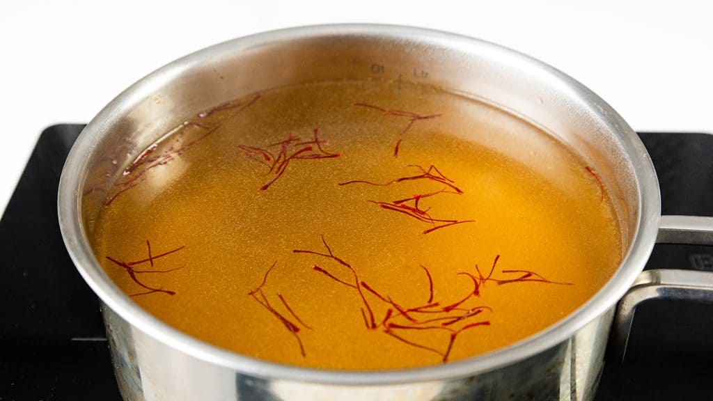 A stainless steel pot filled with golden saffron broth, featuring visible saffron threads, rests on a black stovetop—a perfect start for Easy One Pot Scallops & Chorizo Paella.