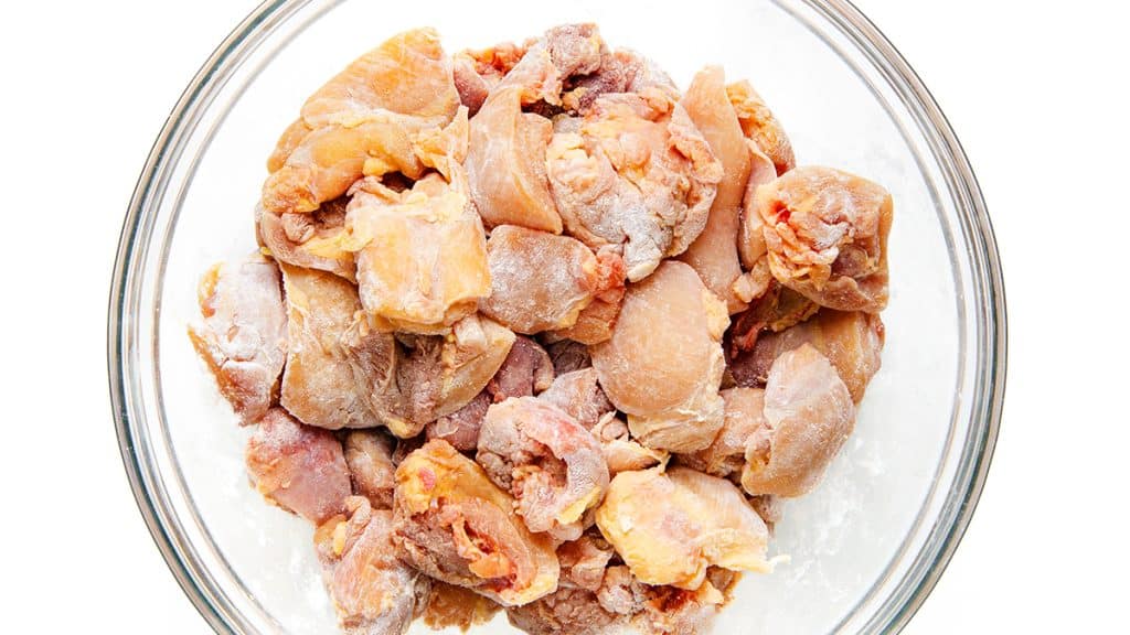 A glass bowl filled with raw, frozen pieces of chicken, perfect for making Slow Cooker Honey Soy Chicken, viewed from above on a white background.