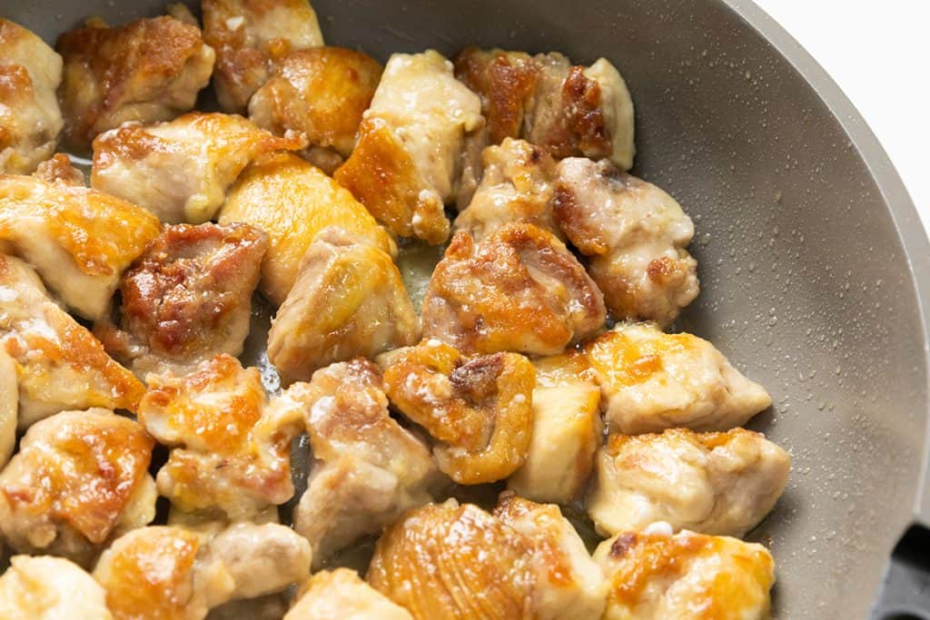 Close-up of golden brown chicken pieces being cooked in a frying pan, with crispy edges and juicy texture, reminiscent of Slow Cooker Honey Soy Chicken.