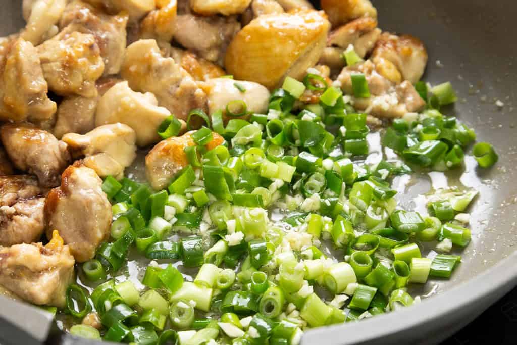 Chopped green onions and pieces of cooked chicken are being sautéed together in a pan with oil and garlic, similar to the flavors found in Slow Cooker Honey Soy Chicken.