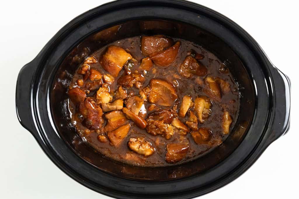 A black slow cooker filled with a hearty stew, similar to Slow Cooker Honey Soy Chicken, featuring chunks of meat and potatoes in a rich brown sauce, viewed from above on a white background.