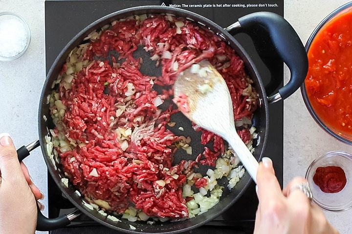 A pan with ground beef browning with a wooden spoon