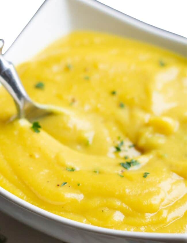 A bowl of bright yellow cauliflower soup in a white bowl