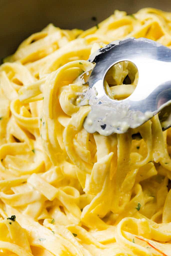 Close-up of creamy Tagliarini with Saffron Cream Sauce being lifted with a metal pasta server, highlighting the rich, golden sauce coating each noodle.