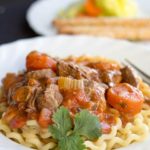 A plate of Italian Lamb Stew on a bed of pasta with a fork