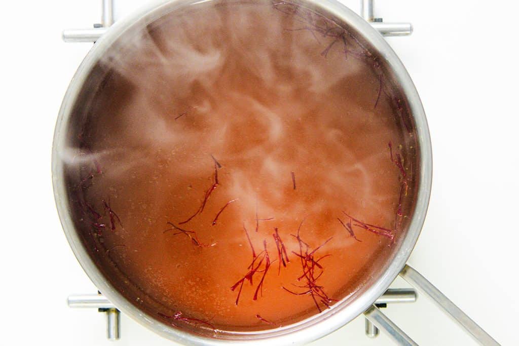 A pot of steaming Low Fat Creamy Cauliflower Saffron Soup with thin saffron threads floating on the surface, viewed from above on a white background.