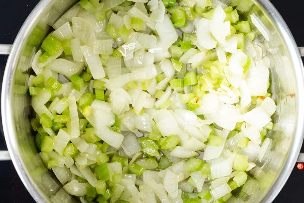 Chopped onions and celery are saut&eacute;ing in a silver pot, viewed from above, with the vegetables turning translucent and glossy&mdash;the perfect base for Low Fat Creamy Cauliflower Saffron Soup.