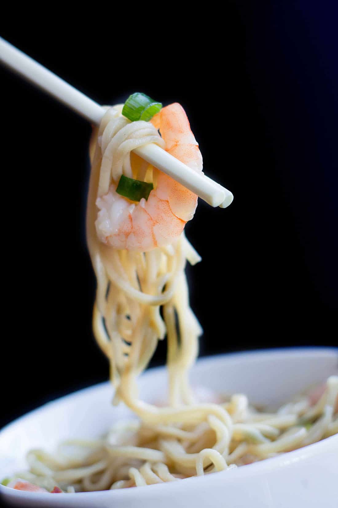Chopsticks holding noodles and a whole shrimp from the soup