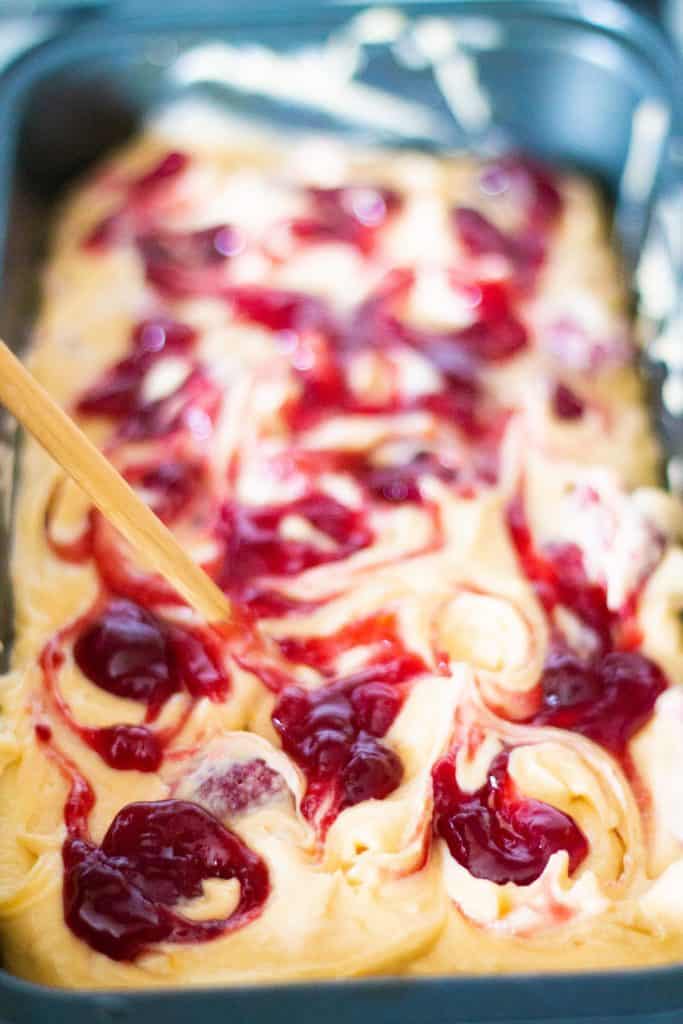 jam being swirled into cake batter in a loaf tin