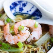A bowl of Chinese Shrimp noodle soup with scattered chili flakes and sliced green onions