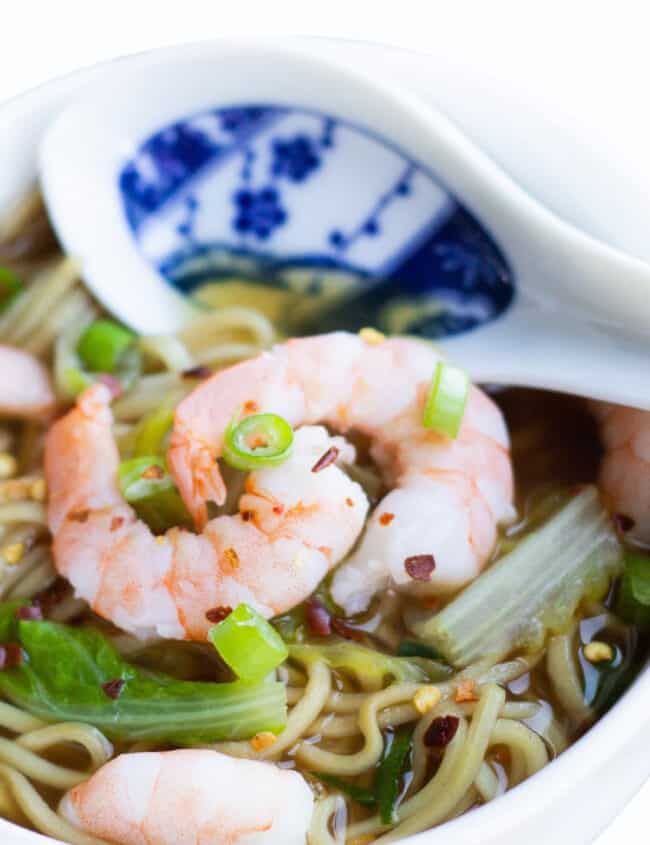 A bowl of Chinese Shrimp noodle soup with scattered chili flakes and sliced green onions