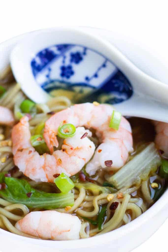 A bowl of Chinese Shrimp noodle soup with scattered chili flakes and sliced green onions