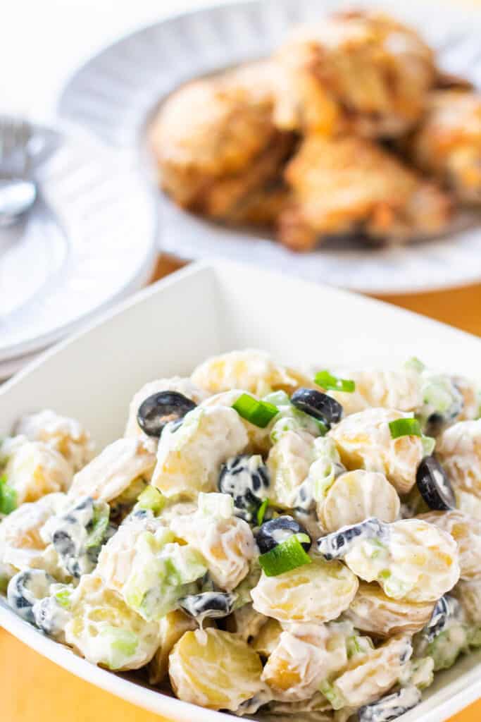 a bowl of potato salad with chicken in the background