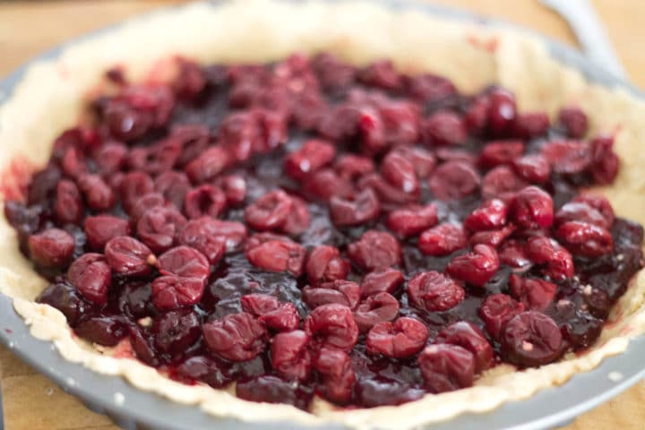 cooked cherries on top of raw pastry in a round pan