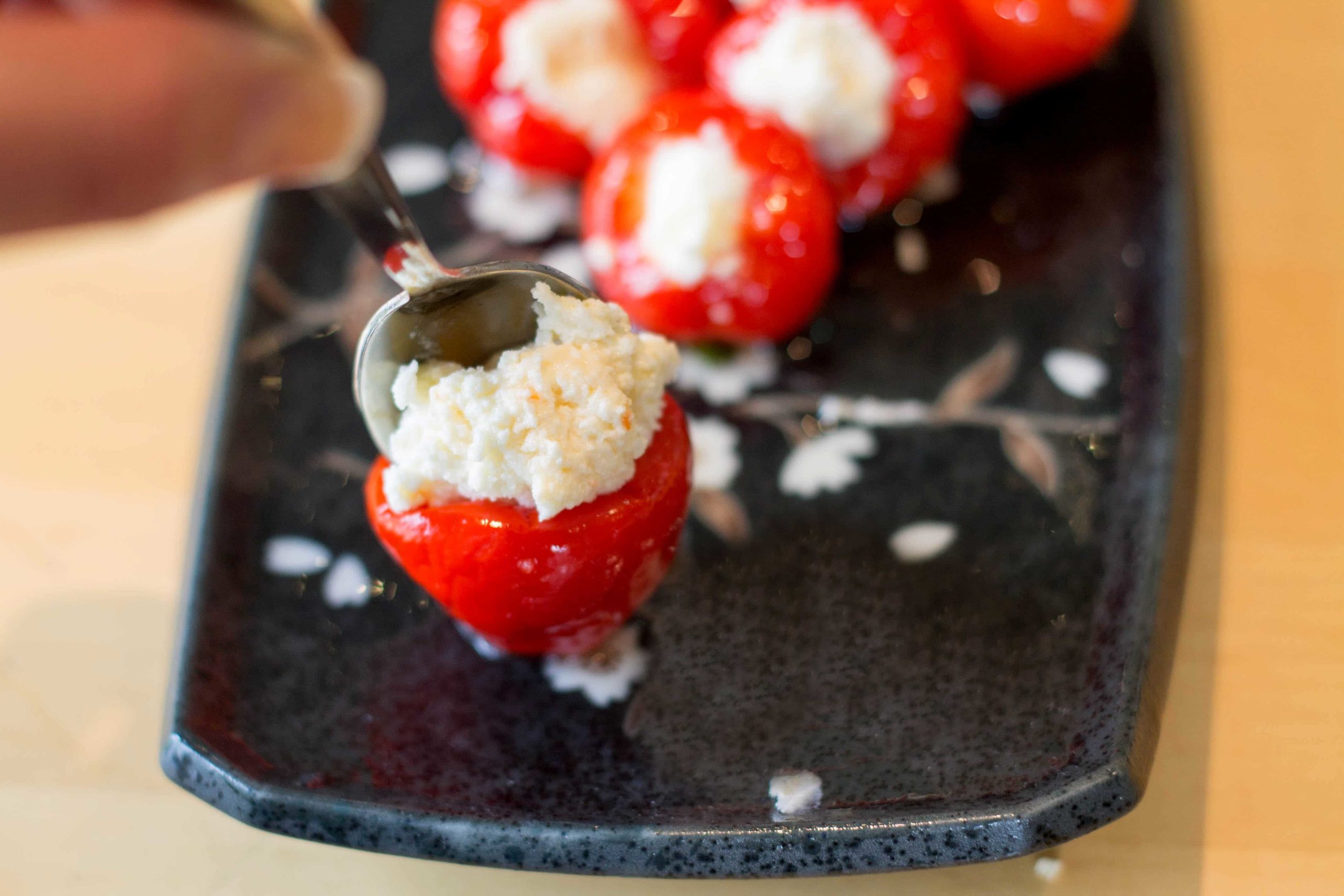 Peppers being filled with spoonfuls of cream cheese