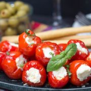 a plate of cream cheese stuffed peppadews with a sprig of basil and a bowl of olives in the background