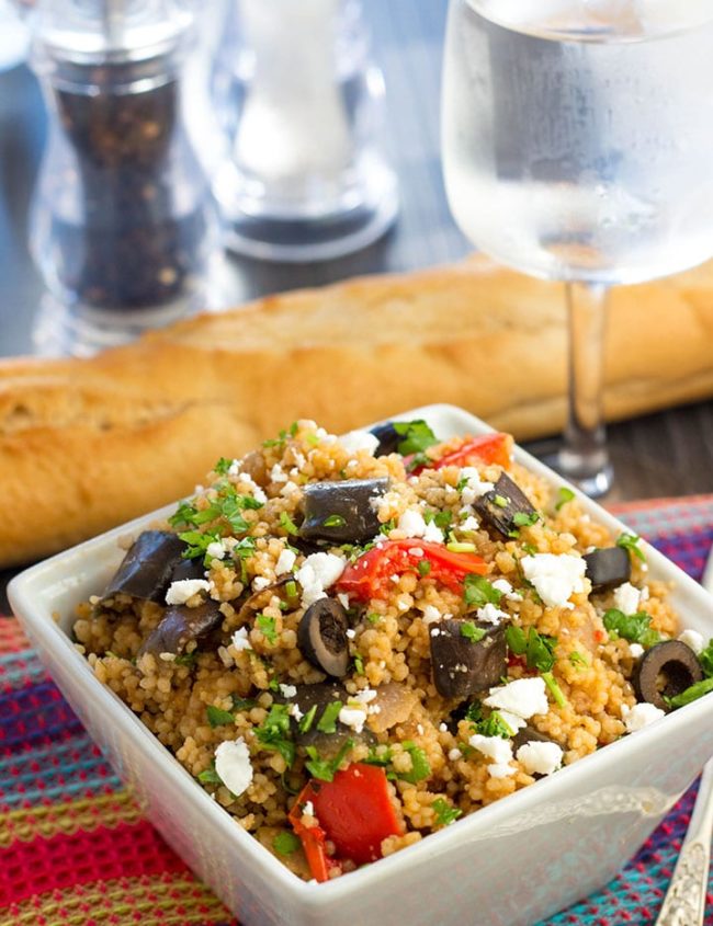 Mediterranean Couscous Salad with Roasted Eggplant in a bowl with a loaf a bread and wine glass on the table in the background