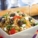 Mediterranean Couscous Salad with Roasted Eggplant in a bowl with a loaf a bread and wine glass on the table in the background
