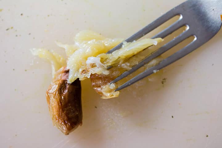 A fork mashing the roasted garlic