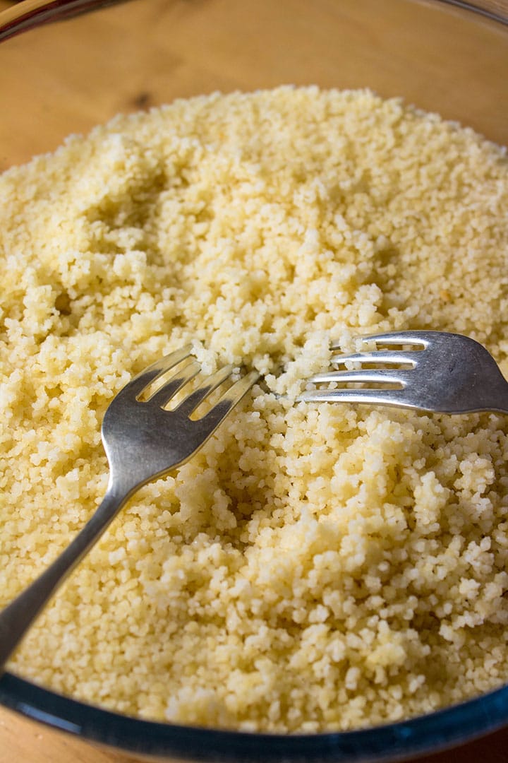 The couscous being fluffed with two forks 