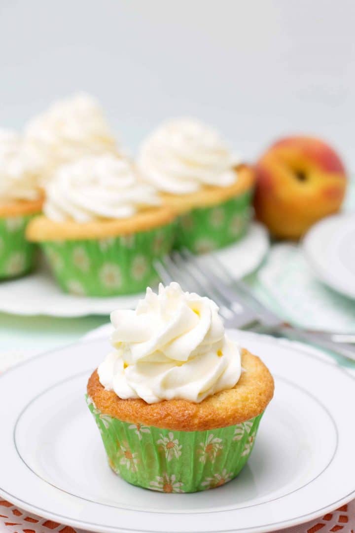 One Peaches and Cream Cupcake on a plate piled high with whipped cream frosting with more cupcakes in the background