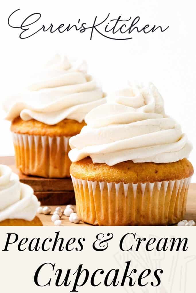 Two cupcakes topped with swirls of creamy frosting sit on a wooden board, perfectly capturing the essence of Peaches and Cream Cupcakes. The text reads “Erren’s Kitchen Peaches & Cream Cupcakes,” while white and peach-colored candies are scattered nearby.