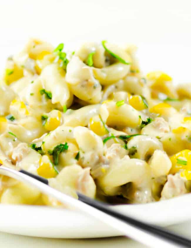 a plate piled high with tuna pasta salad with corn and herbs and a fork next to the plate