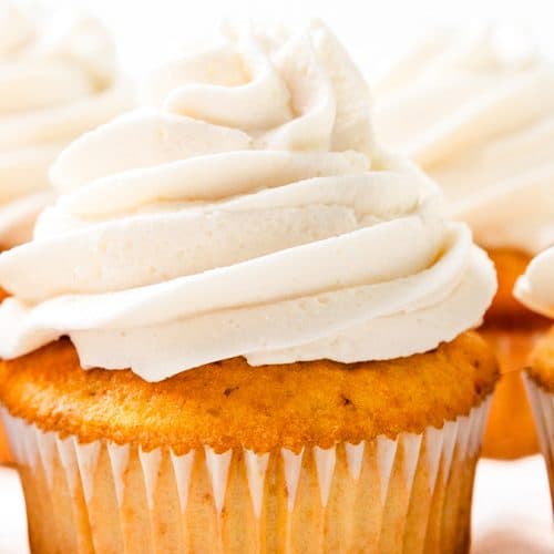 Five Peaches and Cream Cupcakes with swirls of white frosting on top, arranged closely together on a white background.