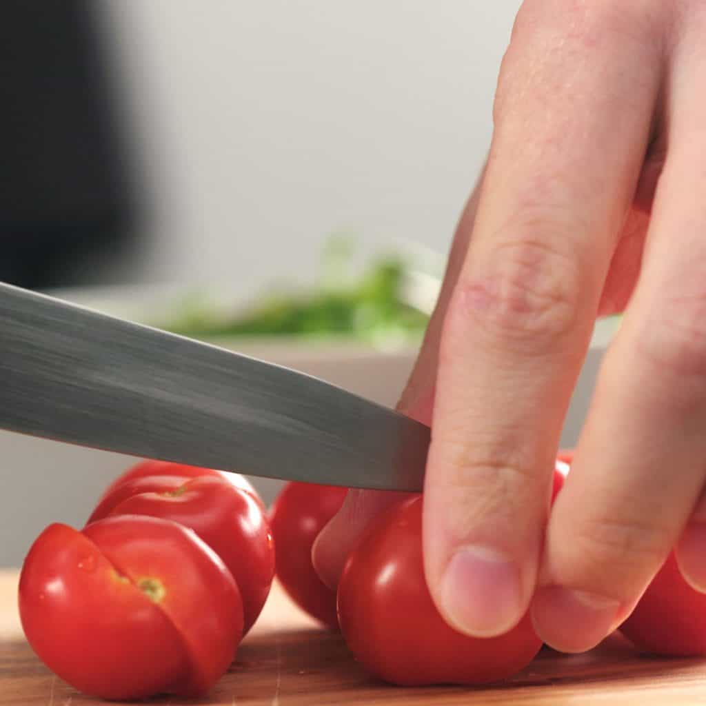 closeup man cutting cherry tomatoes on a cutting board