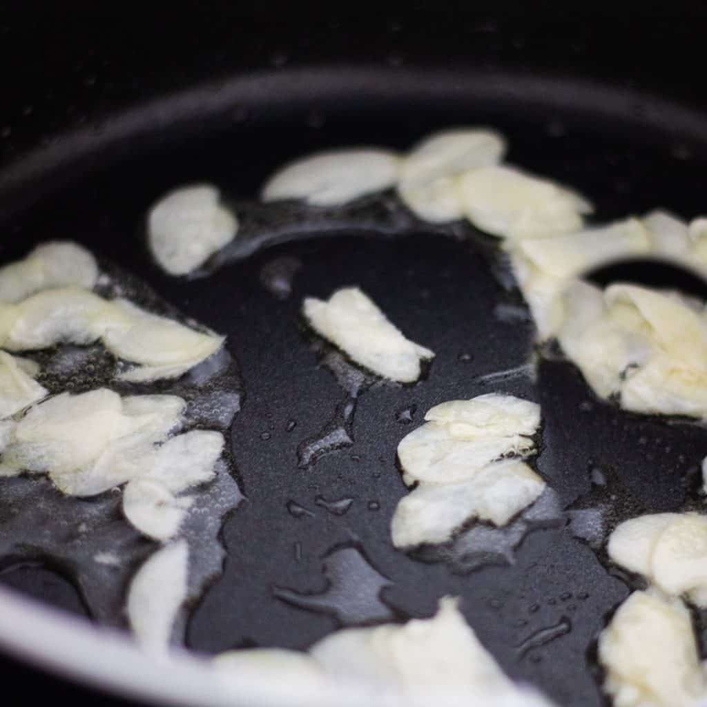 sliced garlic cooking in a pan with oil