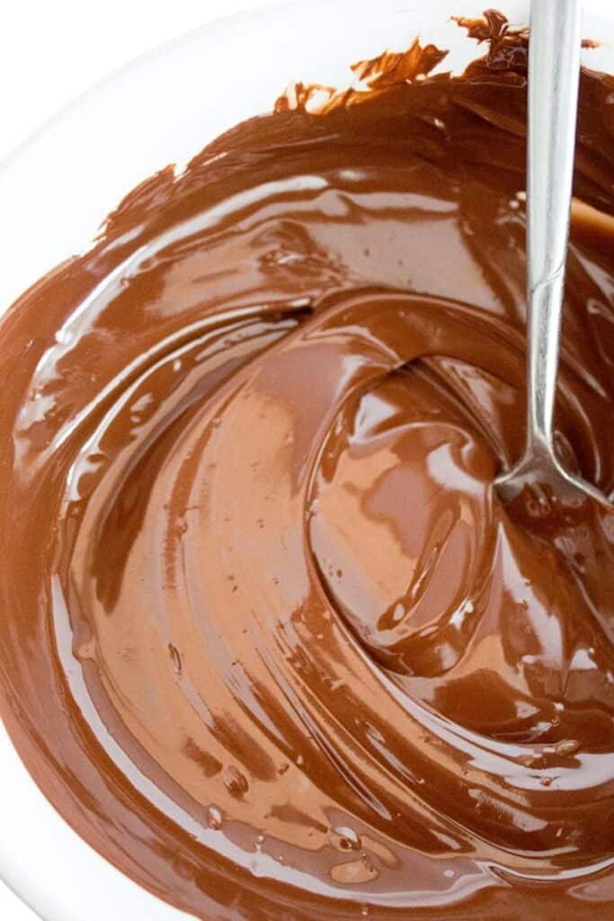 Melted chocolate being stired by a spoon in a white bowl