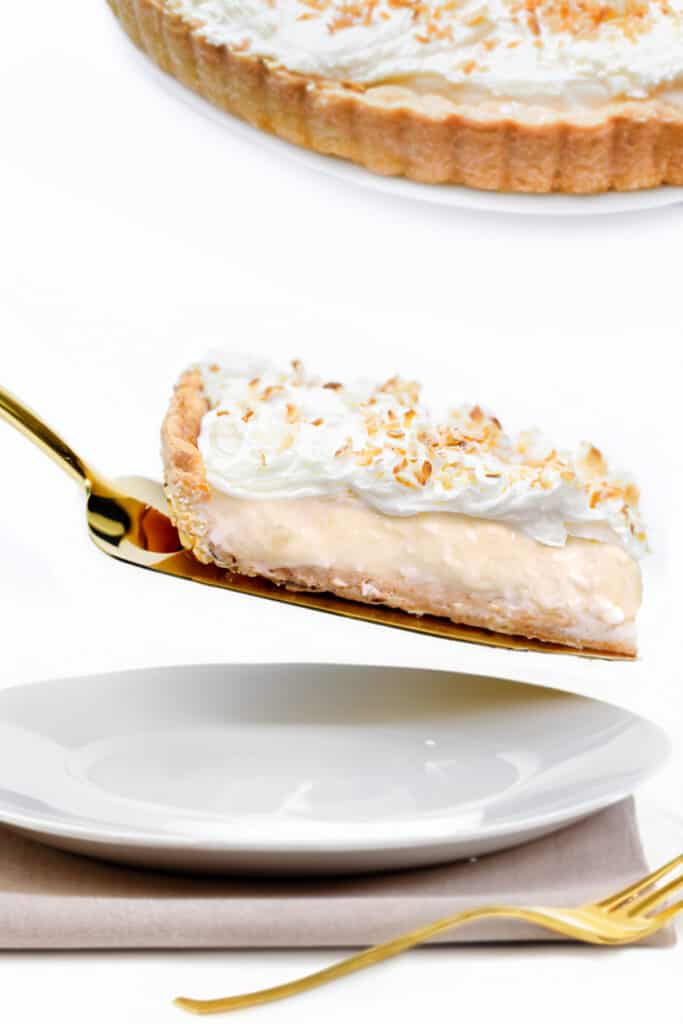 a slice of coconut cream pie being served on a plate with a gold pie server.