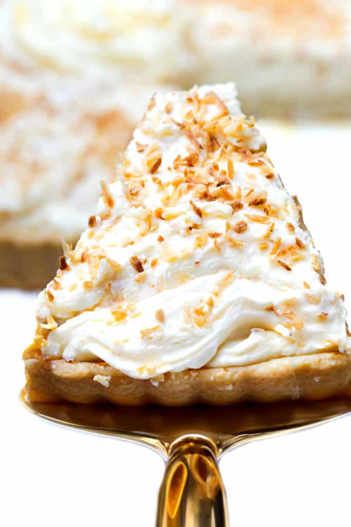 An overhead detailed shot of a slice of coconut cream pie garnished with toasted coconut flakes being served.