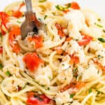 a close up image of a plate of spaghetti with crab, chopped parsley and red peppers