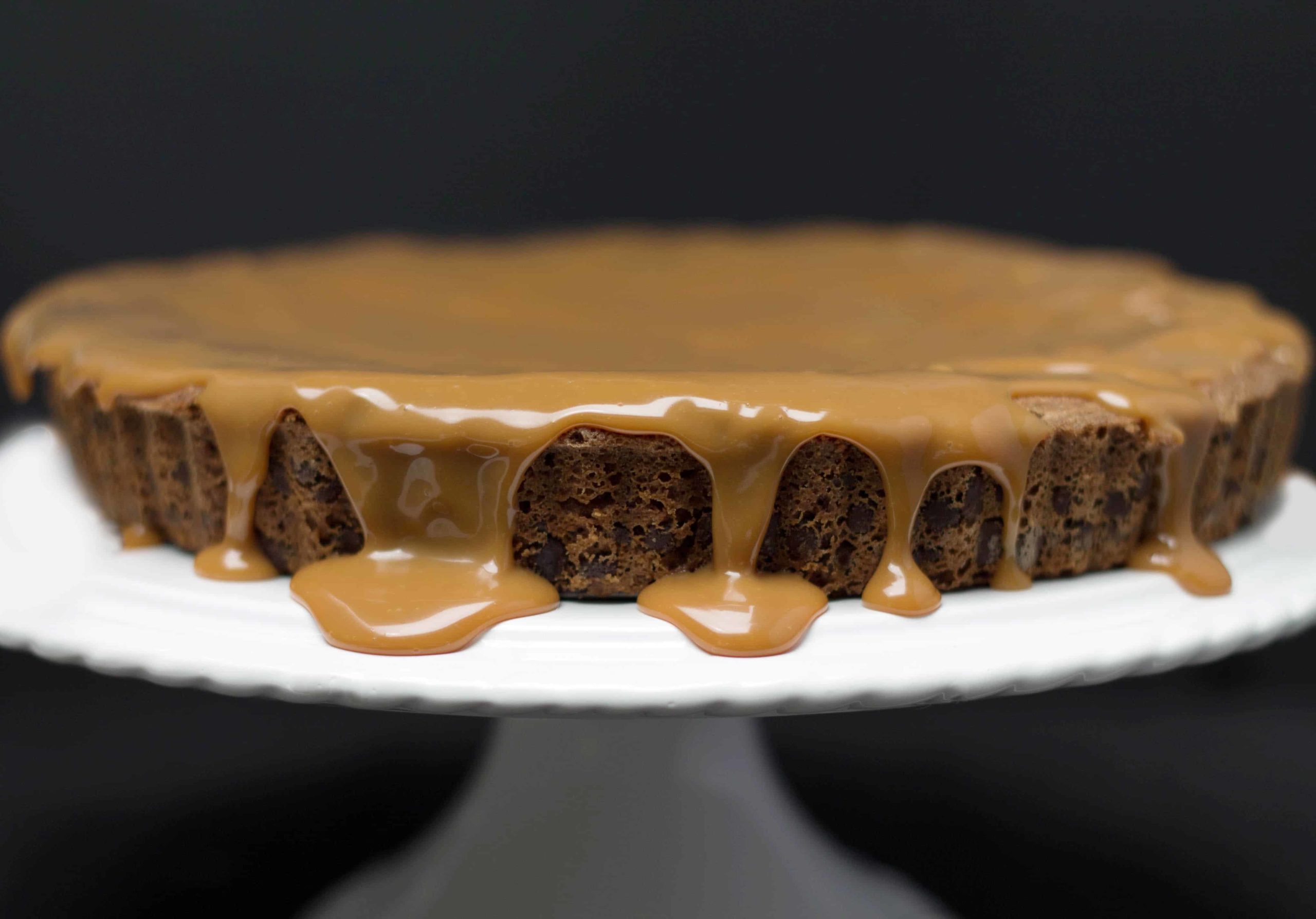 Chocolate Chip Caramel Cake with caramel drizzled over it on a white cake plate