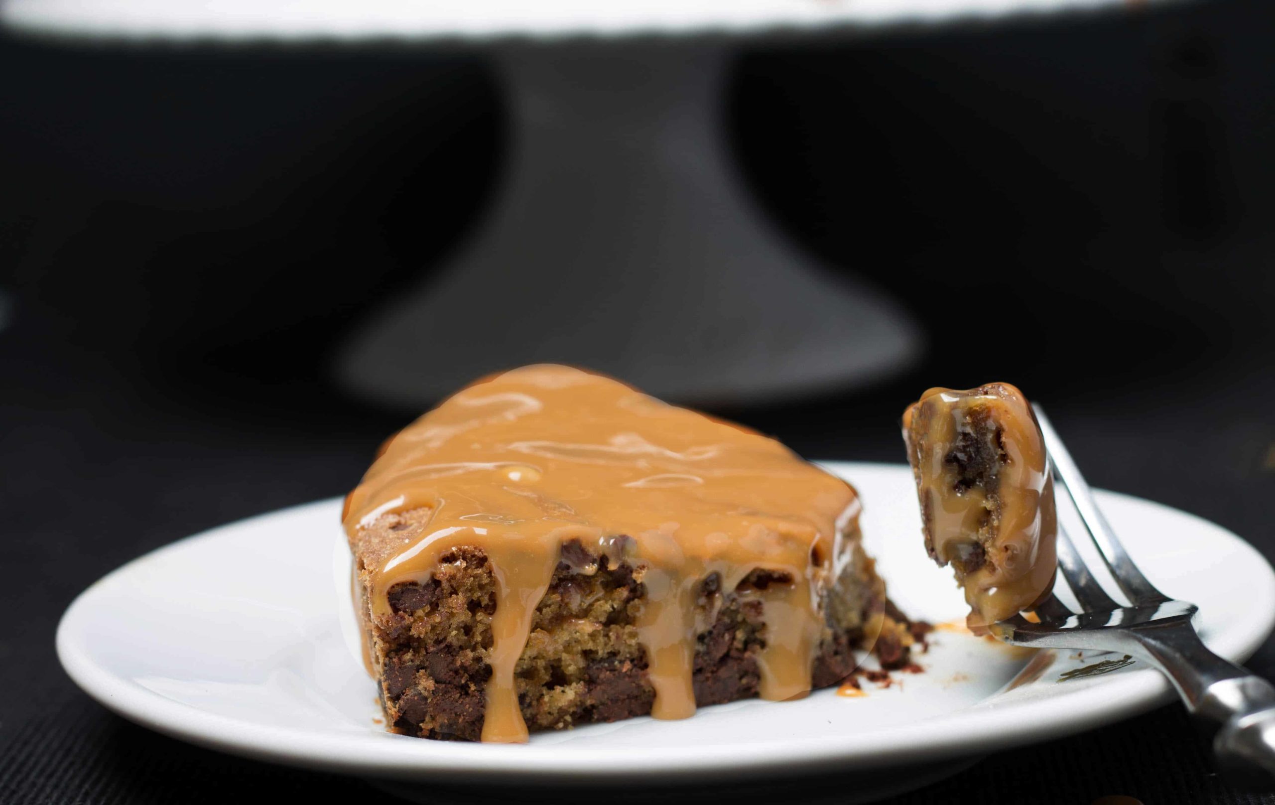 Chocolate Chip Caramel Cake slice on a white plate with a piece of it on a fork beside it