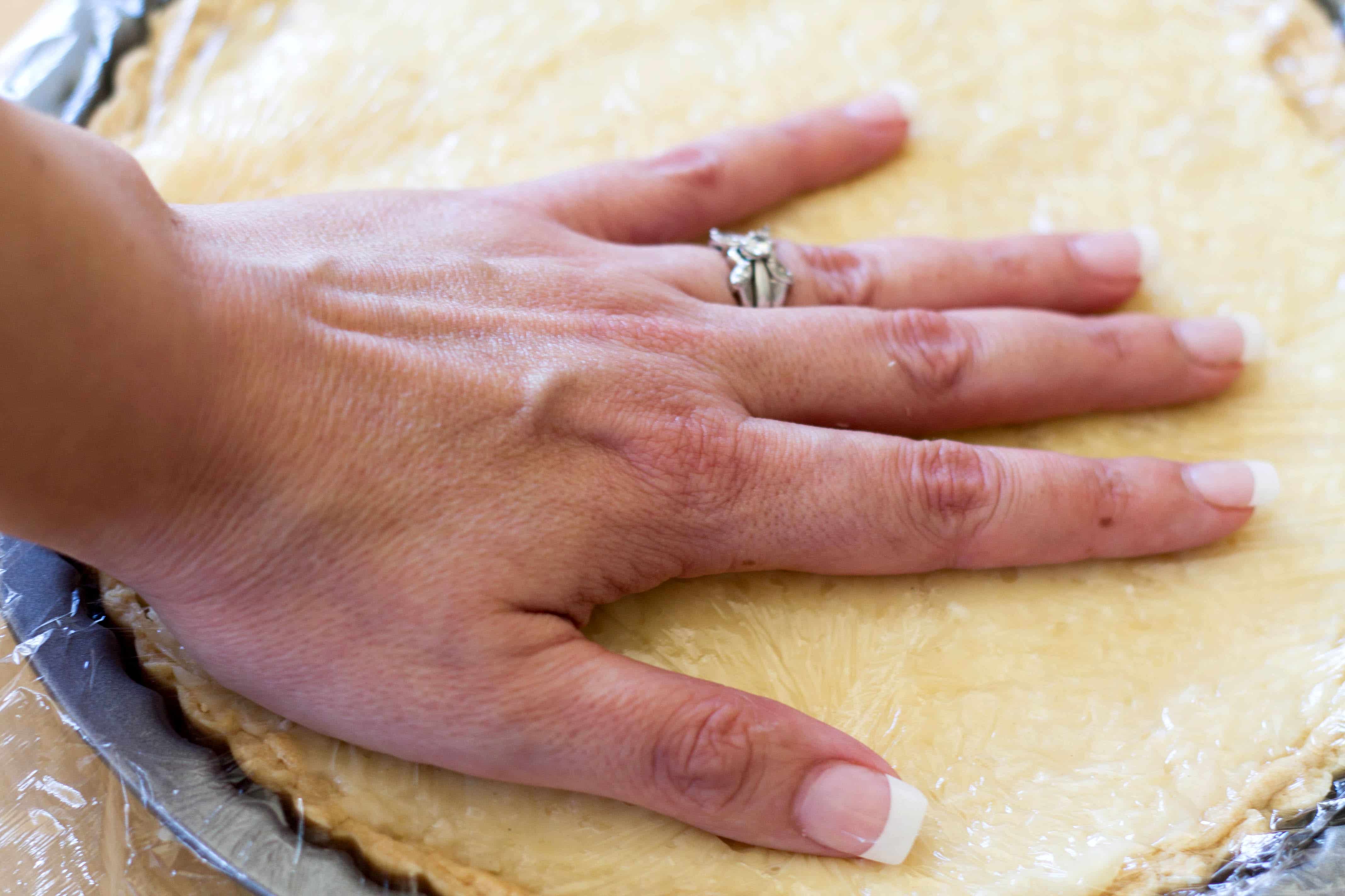 Coconut Cream Pie with plastic being pressed onto the filling