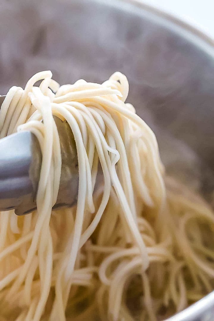 Freshly cooked Chinese noodles being lifted from a pot.