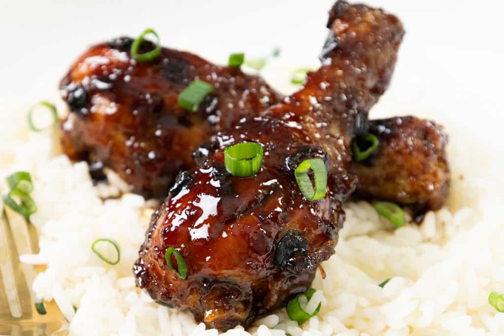 Three sticky Chinese chicken drumsticks glazed to perfection and garnished with chopped green onions, served on a bed of white rice.