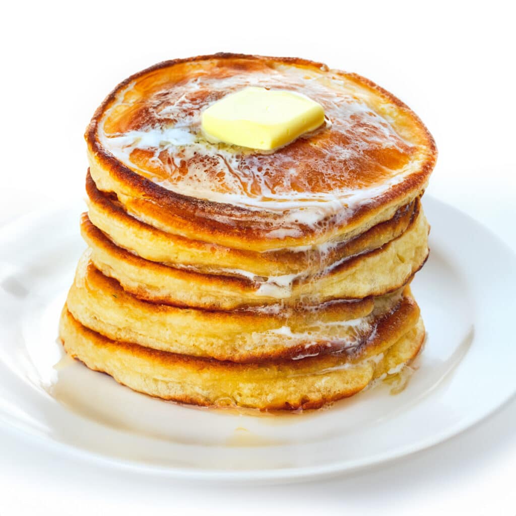 a stack of Scotch pancakes on a white plate topped with butter that's running down the stack.