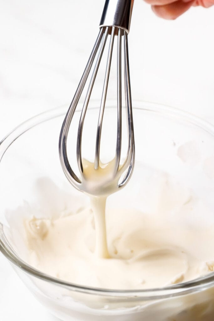 The scotch pancakes batter running off a whisk over the bowl.