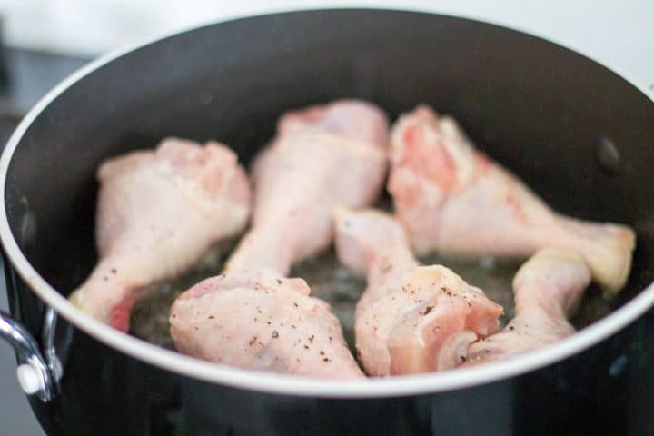 Chicken legs seasoned with salt and pepper being seared in a pan.
